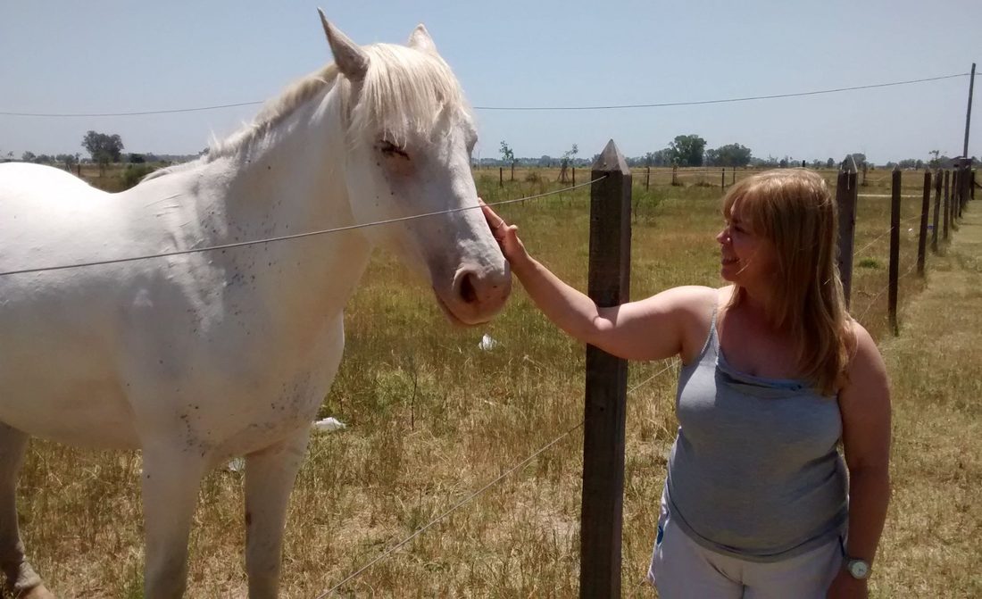 Una integrante del equipo junto a un caballo blanco en el alambrado